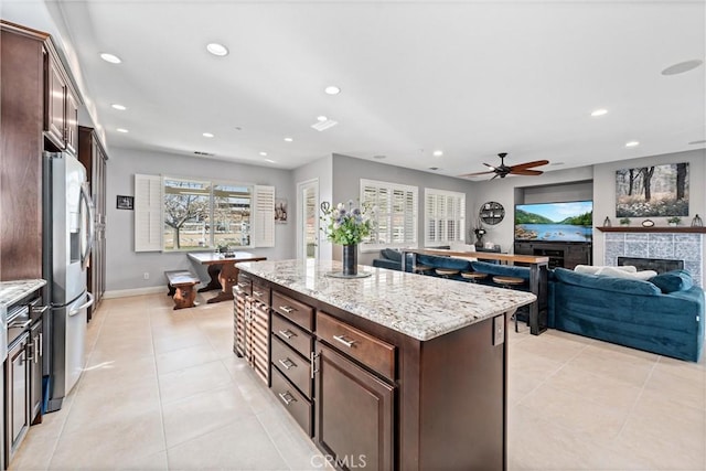 kitchen featuring a kitchen island, recessed lighting, stainless steel fridge with ice dispenser, dark brown cabinetry, and a tiled fireplace