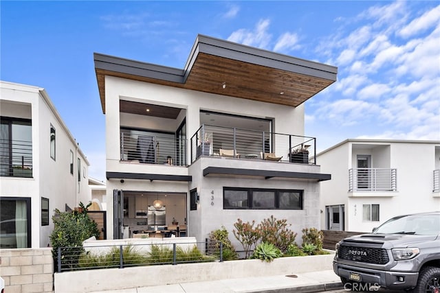 back of house with a balcony, a fenced front yard, and stucco siding