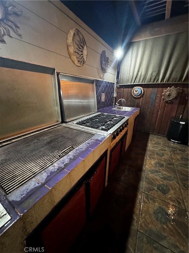 kitchen with a sink, stone finish flooring, wood walls, and decorative backsplash