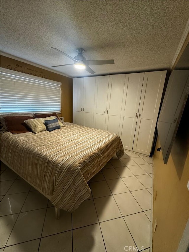 bedroom with ceiling fan, light tile patterned floors, and a textured ceiling