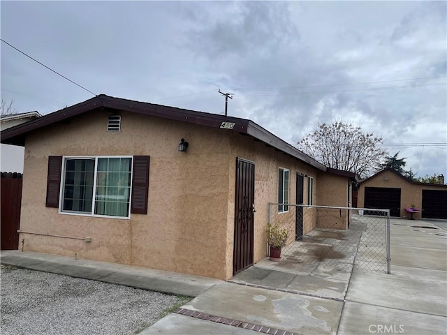 view of property exterior featuring stucco siding, a detached garage, an outdoor structure, and fence