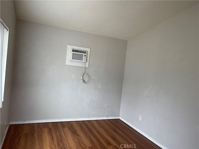 spare room featuring baseboards, a wall unit AC, and wood finished floors