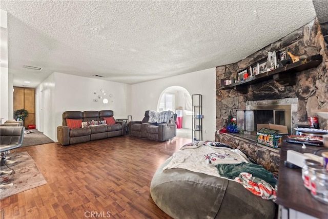 living room featuring visible vents, a textured ceiling, wood finished floors, arched walkways, and a stone fireplace