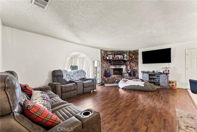 living area featuring wood finished floors, visible vents, a fireplace, arched walkways, and a textured ceiling