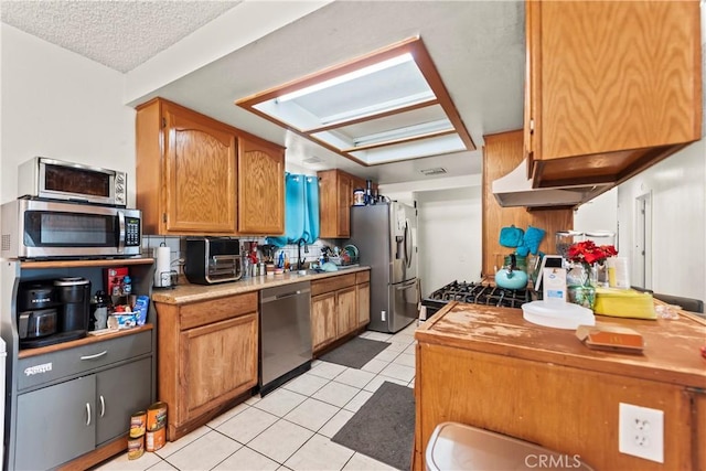 kitchen featuring under cabinet range hood, a sink, a textured ceiling, appliances with stainless steel finishes, and light tile patterned floors