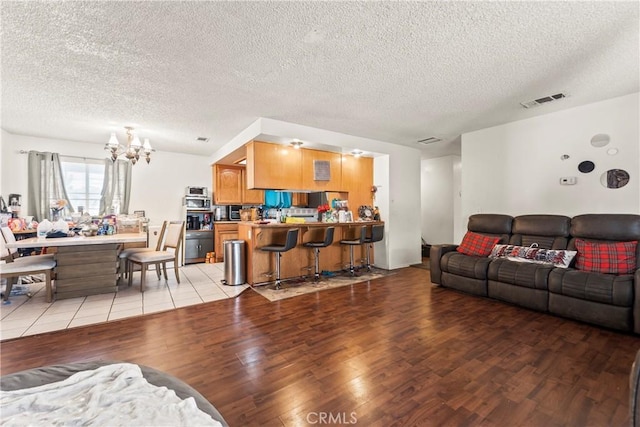 living area featuring light wood-type flooring, visible vents, a notable chandelier, and a textured ceiling