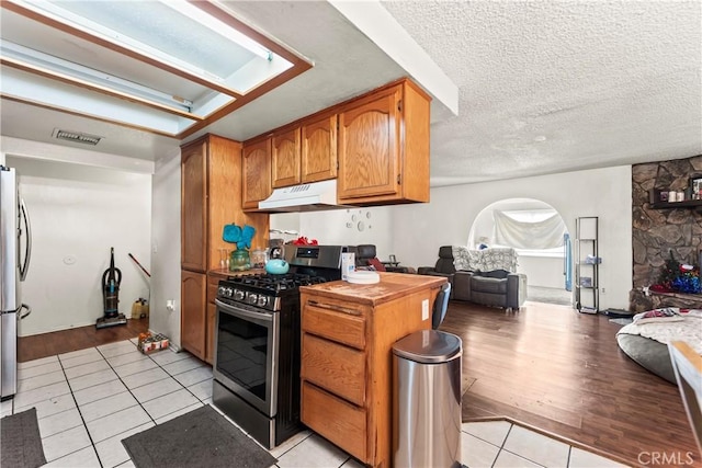 kitchen with under cabinet range hood, stainless steel appliances, arched walkways, and a textured ceiling