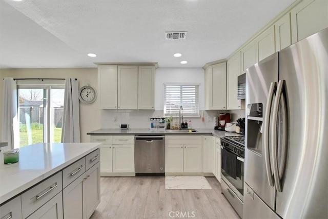 kitchen featuring visible vents, light wood finished floors, a sink, appliances with stainless steel finishes, and backsplash