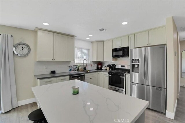 kitchen with a sink, decorative backsplash, light wood-type flooring, and stainless steel appliances