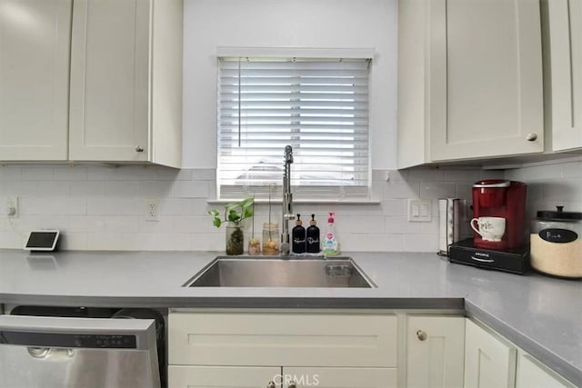 kitchen with backsplash, white cabinetry, stainless steel dishwasher, and a sink