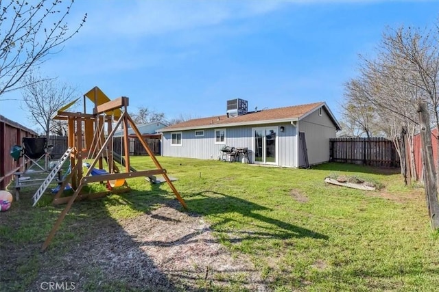 back of house with a yard, central AC, a fenced backyard, and a playground