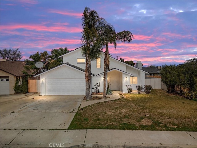traditional home featuring a garage, concrete driveway, fence, a front yard, and stucco siding