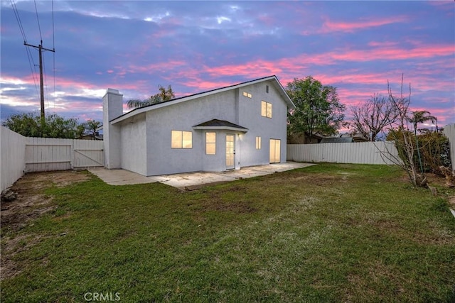 back of property at dusk with a yard, a fenced backyard, and a gate