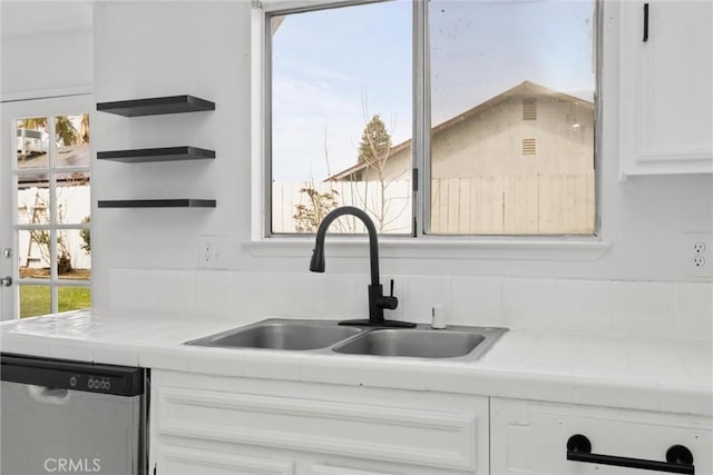 kitchen featuring a wealth of natural light, a sink, stainless steel dishwasher, tile countertops, and white cabinets