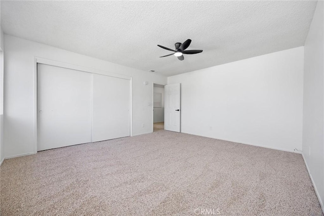 unfurnished bedroom with a textured ceiling, a closet, carpet flooring, and a ceiling fan
