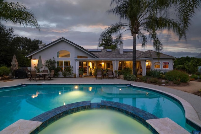 pool at dusk featuring outdoor dining area, a patio, and a pool with connected hot tub