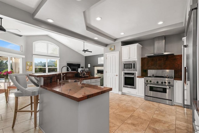 kitchen featuring dark countertops, open floor plan, stainless steel appliances, wall chimney exhaust hood, and a sink