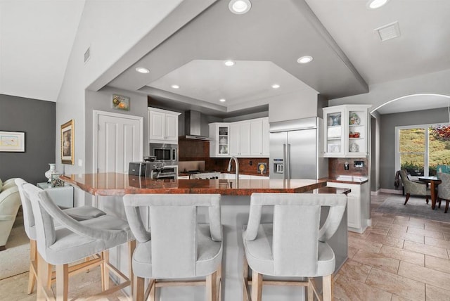 kitchen with visible vents, arched walkways, wall chimney range hood, decorative backsplash, and built in appliances