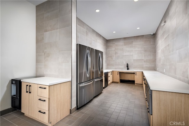 kitchen featuring dark tile patterned flooring, freestanding refrigerator, light brown cabinetry, dishwasher, and tile walls