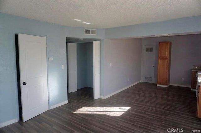 unfurnished bedroom featuring visible vents, baseboards, dark wood-type flooring, and a textured ceiling