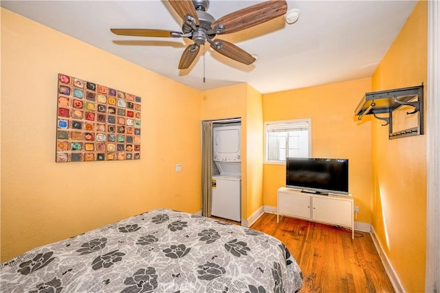 bedroom with stacked washing maching and dryer, a ceiling fan, baseboards, and wood finished floors