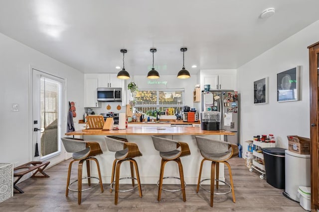 kitchen featuring stainless steel microwave, wood finished floors, white cabinetry, light countertops, and range