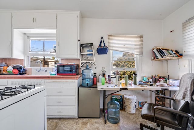 kitchen with black microwave, tile counters, decorative backsplash, freestanding refrigerator, and white cabinets