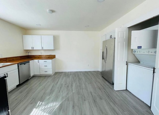 kitchen with wooden counters, appliances with stainless steel finishes, light wood-style floors, white cabinetry, and stacked washer / drying machine