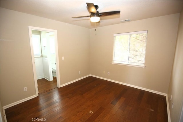 unfurnished room with ceiling fan, visible vents, baseboards, and dark wood finished floors