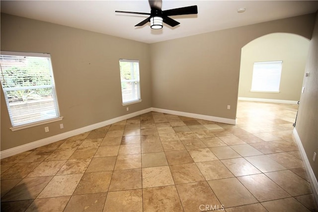 unfurnished room featuring light tile patterned floors, baseboards, arched walkways, and ceiling fan