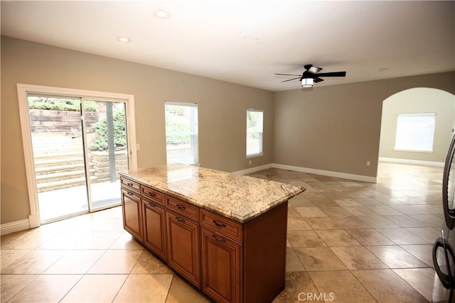 kitchen featuring brown cabinetry, light stone countertops, baseboards, a kitchen island, and arched walkways