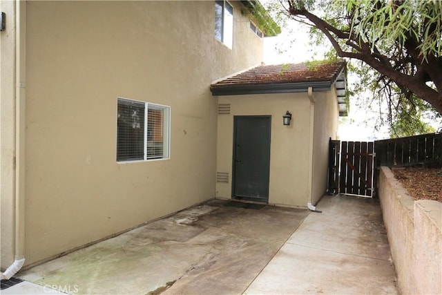 view of exterior entry with stucco siding, a patio, and fence