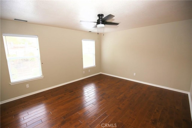 empty room featuring a ceiling fan, visible vents, dark wood-style floors, and baseboards