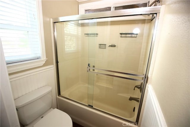 full bathroom with toilet, shower / bath combination with glass door, and wainscoting