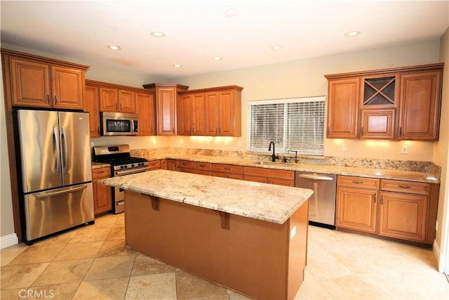 kitchen with light stone counters, brown cabinetry, a kitchen island, a sink, and stainless steel appliances