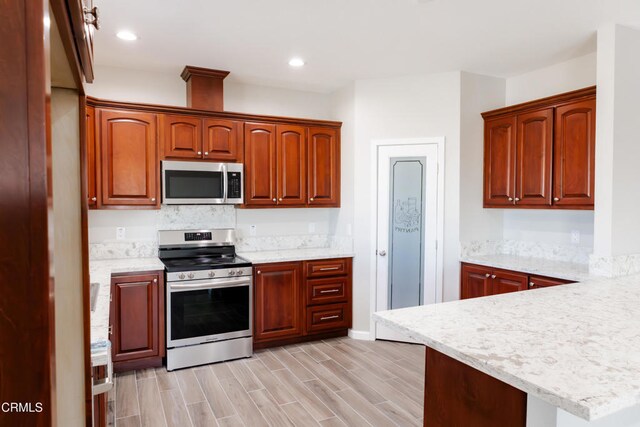 kitchen featuring wood finish floors, stainless steel appliances, a peninsula, and recessed lighting