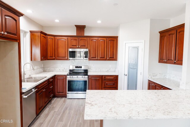 kitchen featuring light wood-type flooring, a sink, recessed lighting, appliances with stainless steel finishes, and a peninsula