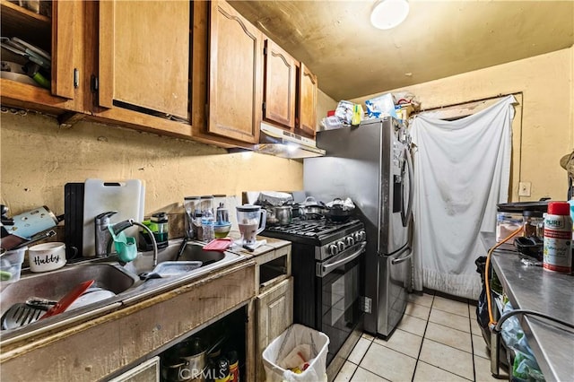 kitchen featuring under cabinet range hood, light tile patterned floors, brown cabinets, stainless steel gas stove, and a sink