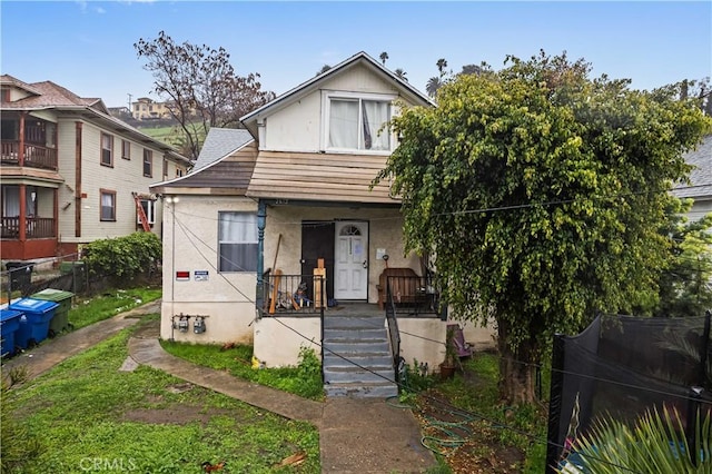 view of front facade featuring stucco siding, a porch, and fence