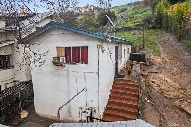 view of property exterior with stucco siding, central AC unit, and fence