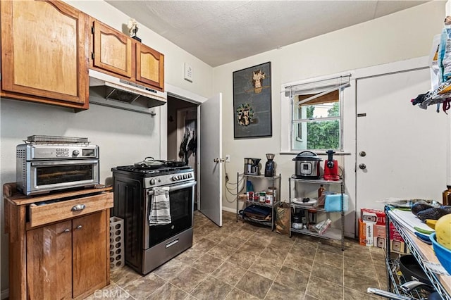 kitchen with under cabinet range hood, a textured ceiling, brown cabinetry, a toaster, and gas range