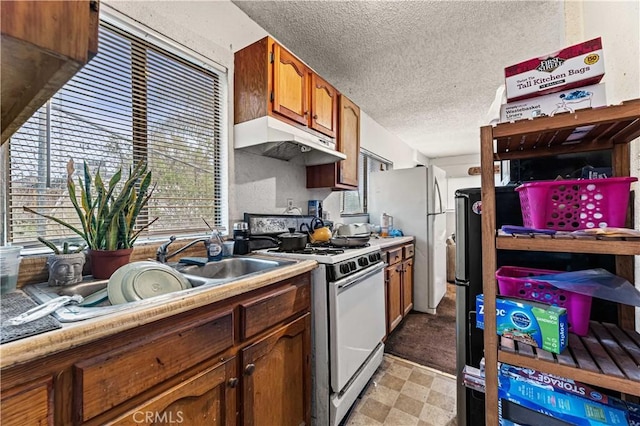 kitchen featuring under cabinet range hood, light floors, brown cabinetry, white appliances, and a textured ceiling