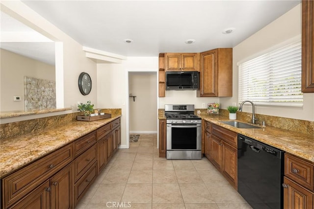 kitchen with light stone counters, light tile patterned floors, brown cabinets, black appliances, and a sink