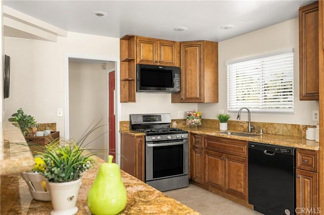 kitchen featuring a sink, light stone counters, black appliances, and brown cabinetry