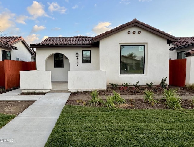 mediterranean / spanish house featuring a tiled roof, stucco siding, a front lawn, and fence