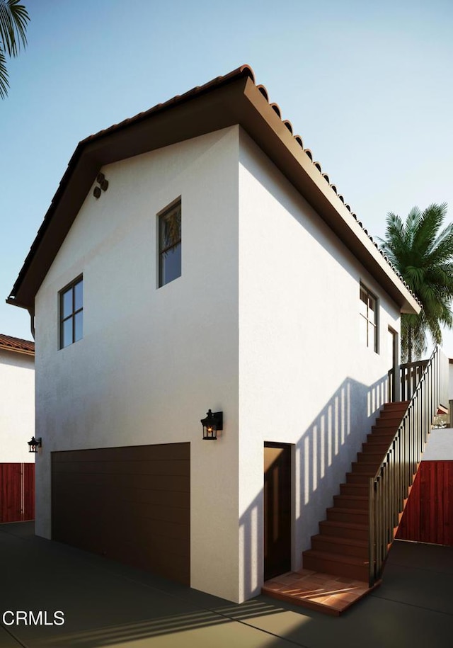 view of side of home featuring stairway, a garage, and stucco siding