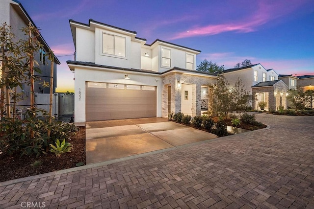 view of front of house with decorative driveway, fence, a garage, and stucco siding