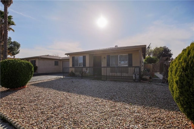 ranch-style home featuring stucco siding, a porch, driveway, and fence