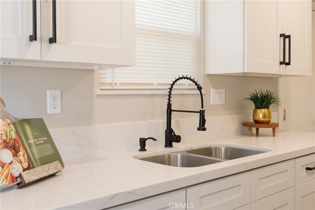 details with white cabinetry, light stone countertops, and a sink