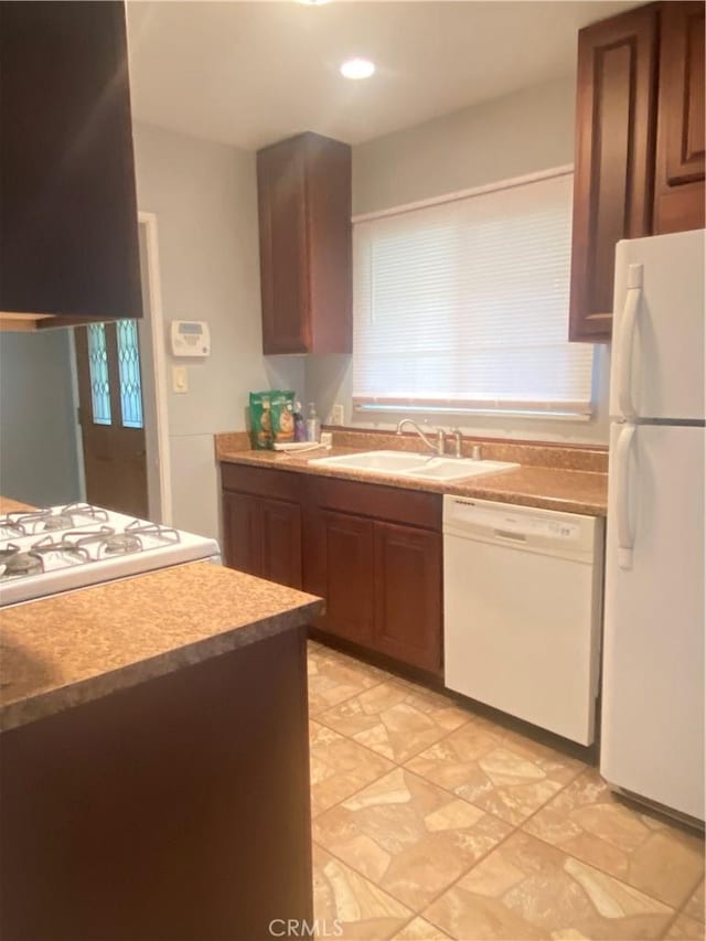 kitchen with a sink, white appliances, brown cabinets, and light countertops